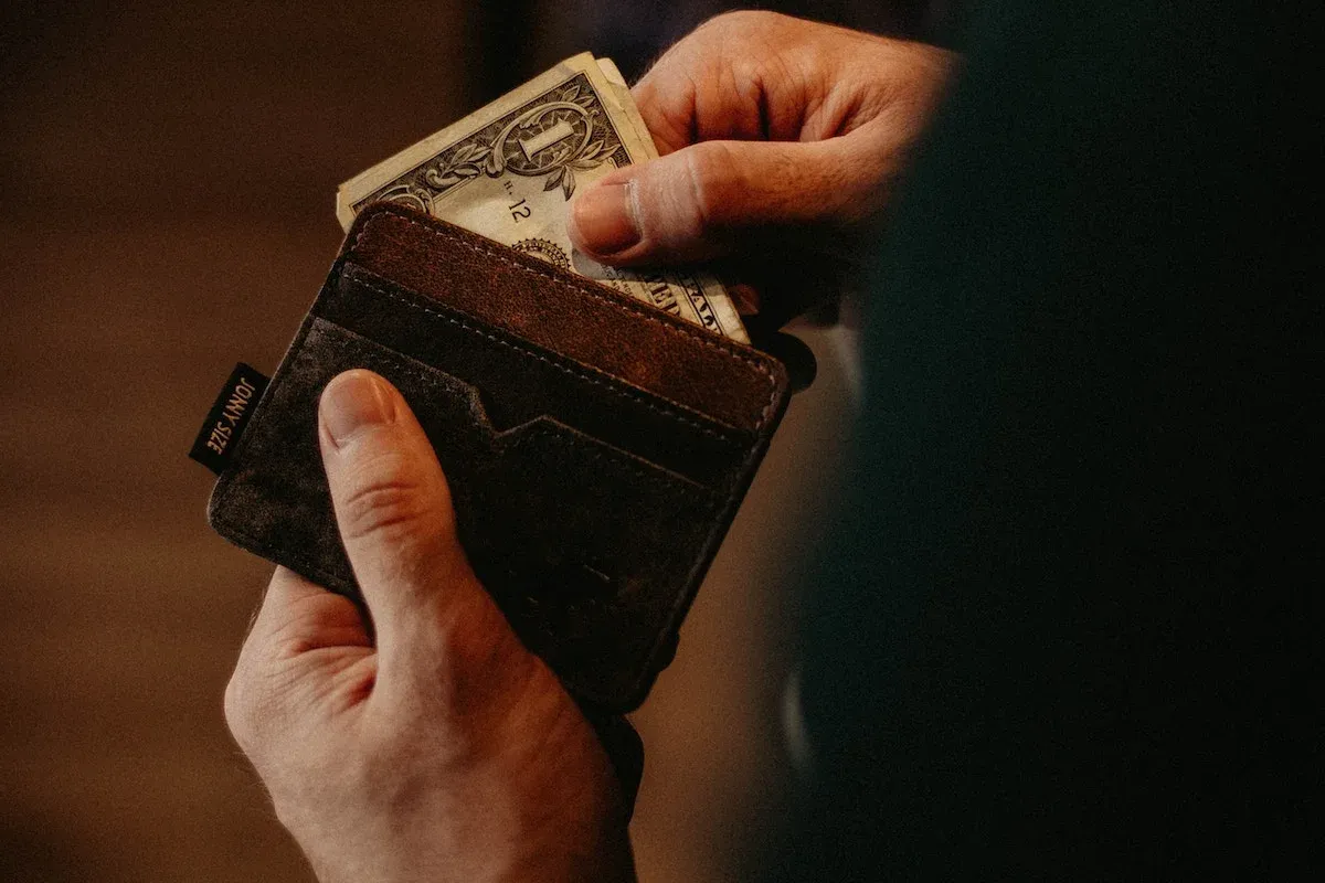 A person holding a leather purse and pulling out a few bills