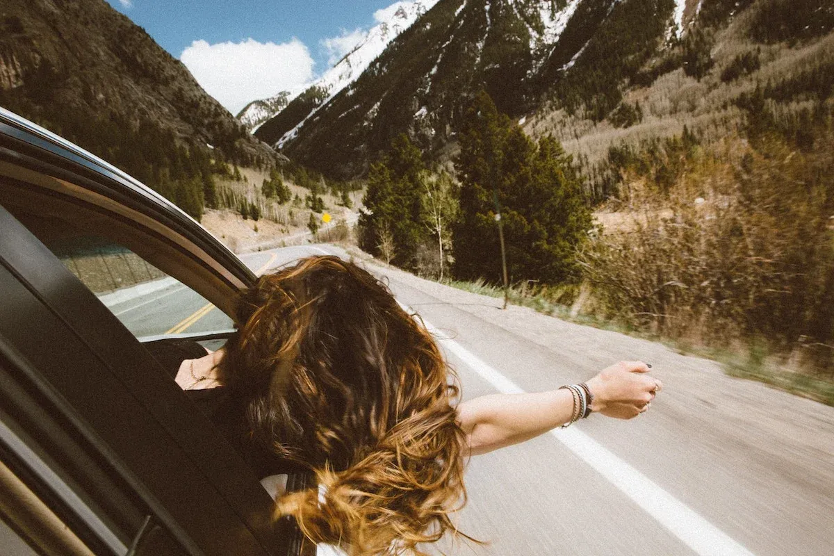 A female car passenger sticks her head and arm out the window